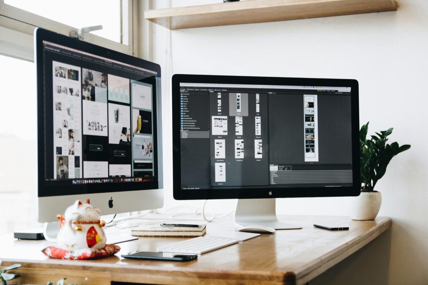 A workspace with two monitors displaying design projects and a cup on the desk.