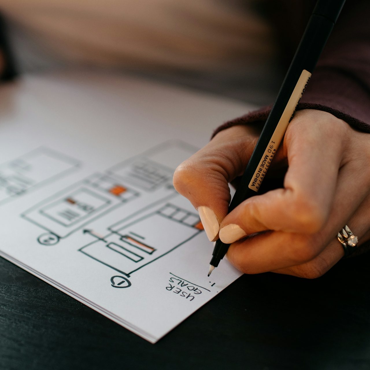 A person sketches a diagram on paper with a pen, focusing on design elements.