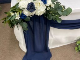 Floral arrangement with blue and white flowers draped over a navy fabric.